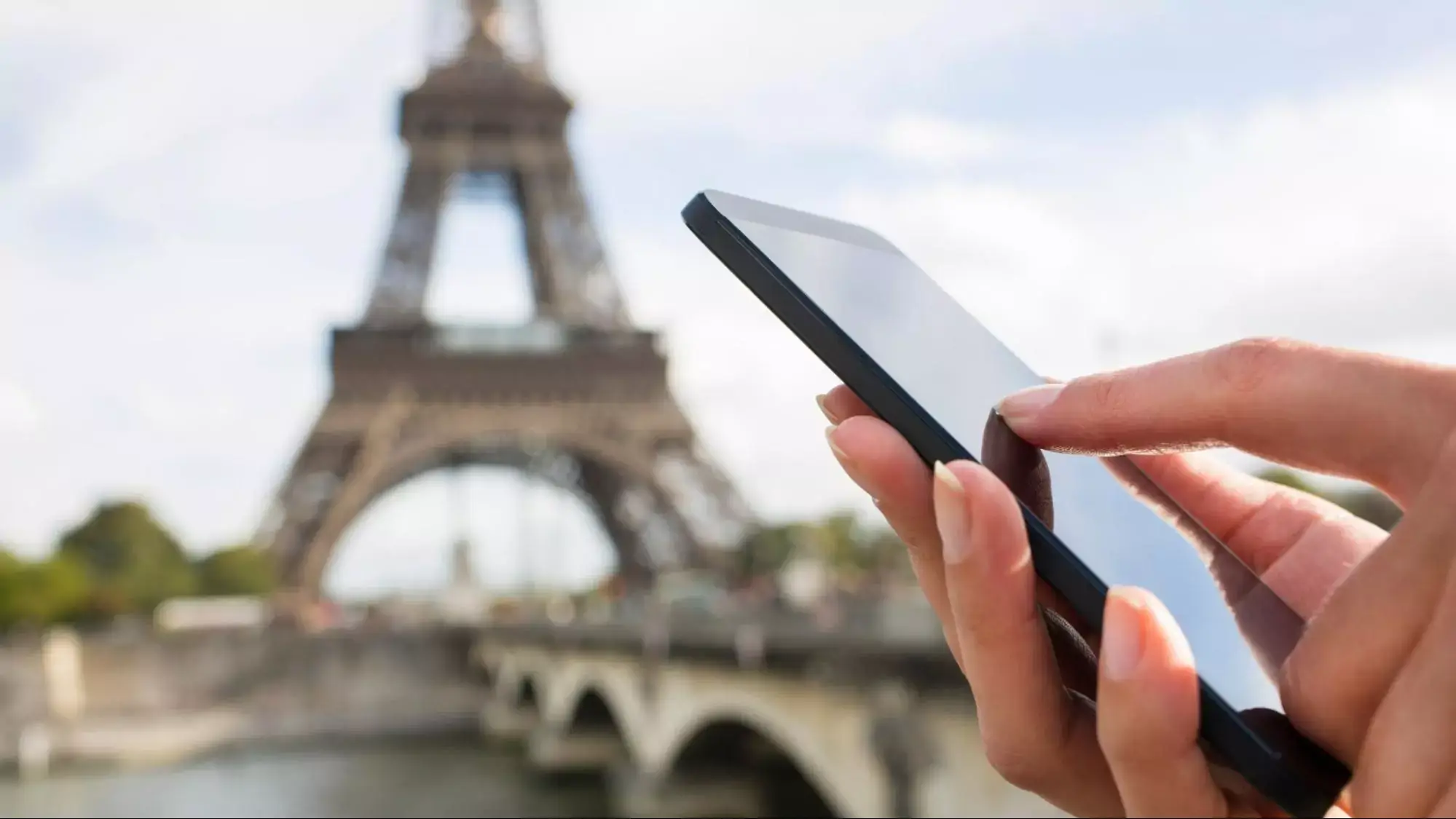 A person holding a mobile device with the Eiffel tower in the background.