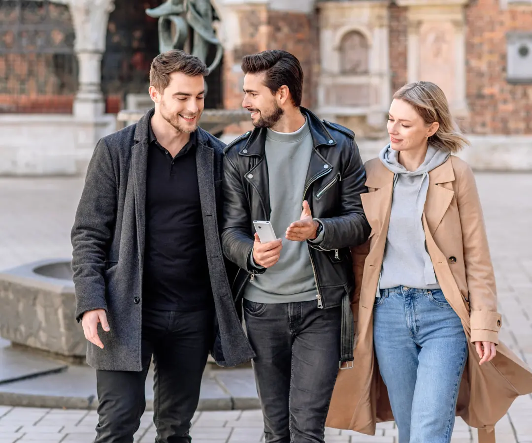 A man holds a translator in his hand and is surrounded by friends. In the background, historic architecture is visible